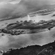 In a photo taken by a Japanese pilot, a plume of water rises from a torpedo that struck USS West Virginia (BB 48) moored on battleship row on the far side of Ford Island. A Japanese aircraft can be seen wheeling over the island, while another flies over the Navy Yard at the top right of the photo. Struck by six torpedoes and two bombs, West Virginia was salvaged, refitted, and took part in the Battle of Leyte Gulf in 1944 and was present for the signing of the Japanese surrender in Tokyo Bay on September 2, 1945. (US Navy)